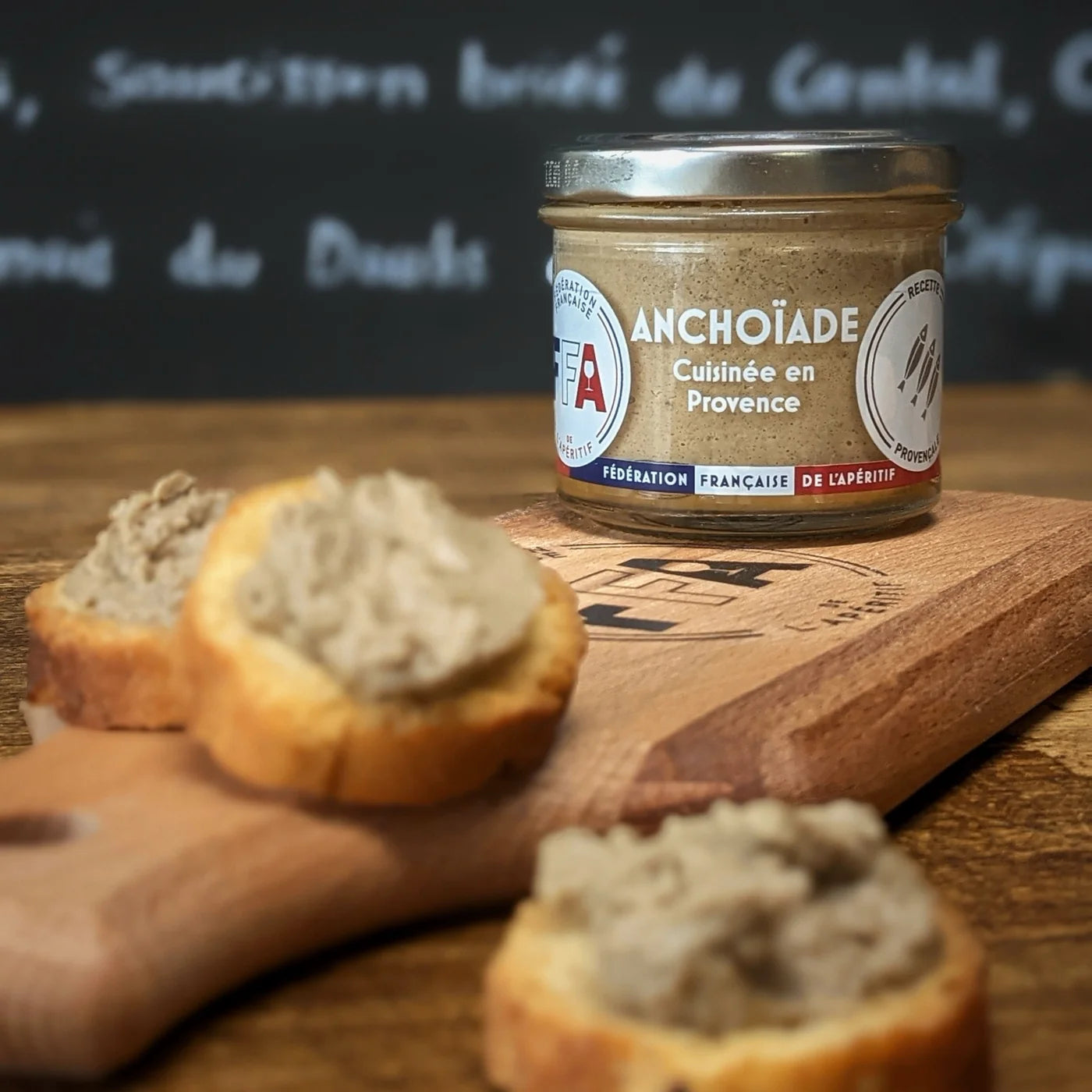 Bocal d’anchoïade FFA cuisinée en Provence posé sur une planche en bois avec toasts tartinés — ambiance apéritive artisanale et conviviale.