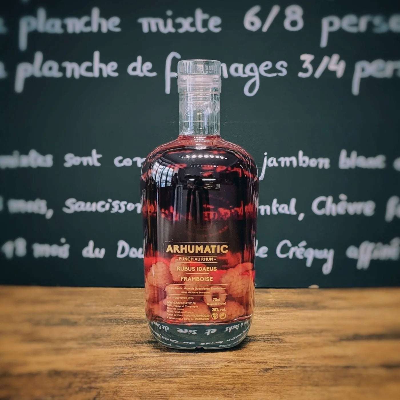 Bouteille d’Arhumatic Framboise posée sur une table en bois, avec ses fruits entiers visibles dans le rhum, ambiance apéritif gourmande et chaleureuse.