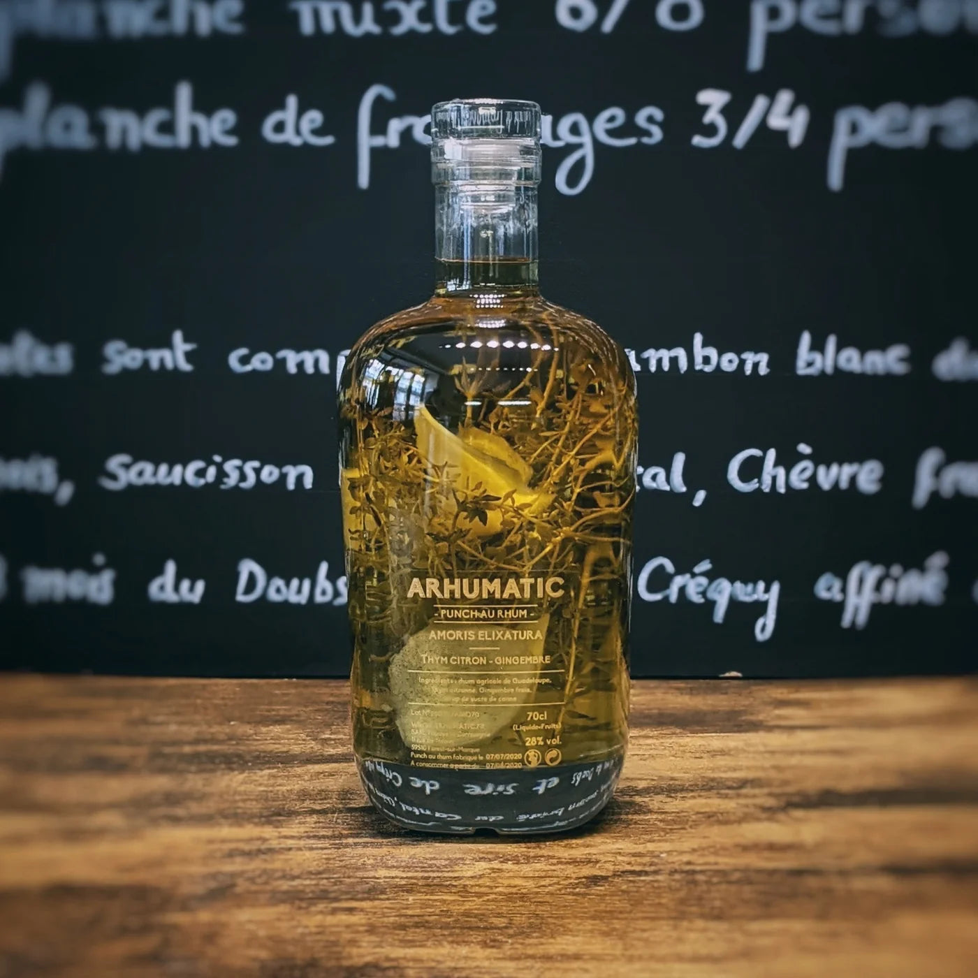 Bouteille d’Arhumatic Thym Citron posée sur une table en bois, laissant apparaître les branches de thym et les quartiers de citron dans le rhum, ambiance apéritif naturelle et raffinée.