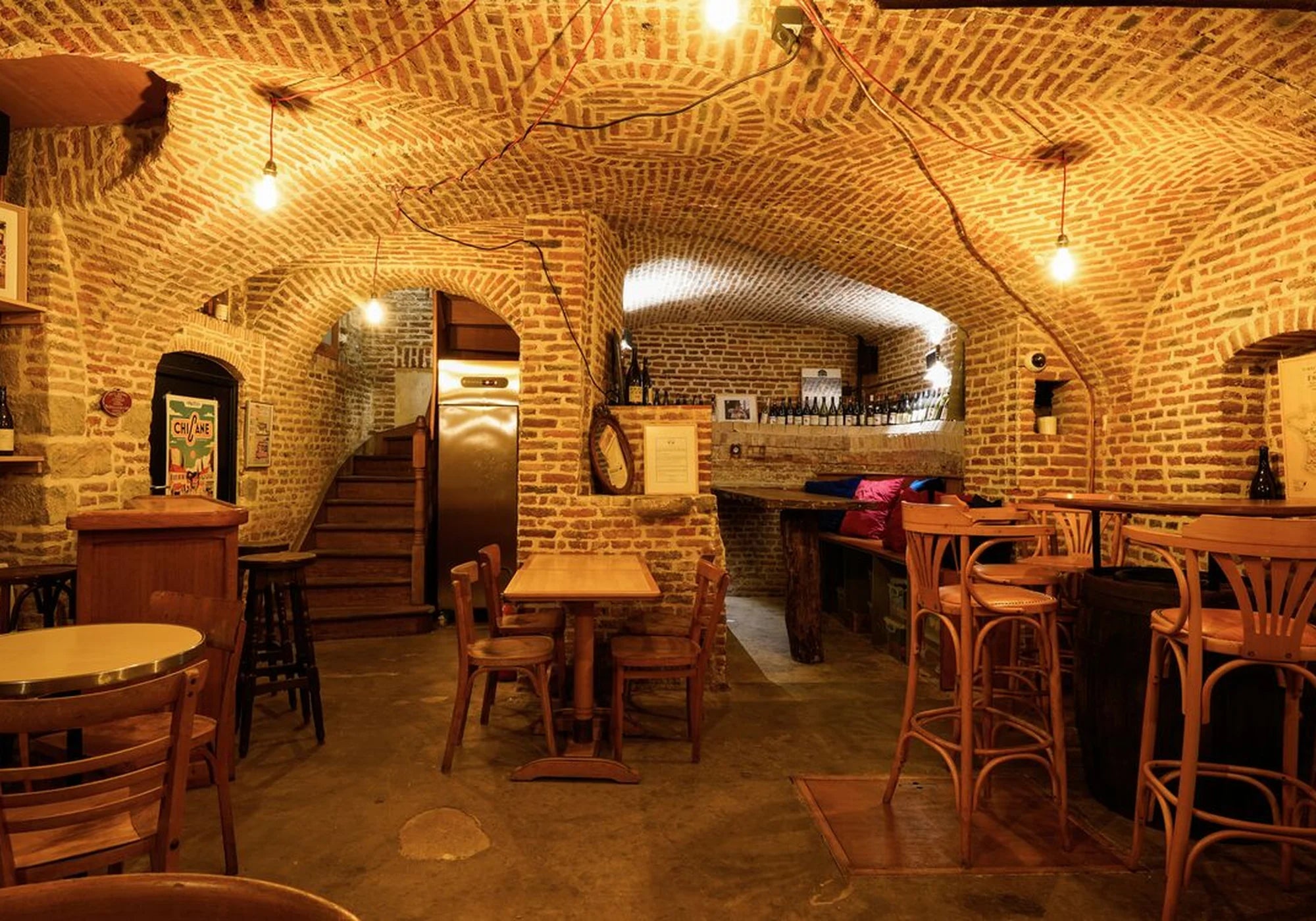 Cave voûtée en briques de la Fédération Française de l’Apéritif aménagée en bar convivial avec tables en bois et lumière chaleureuse.