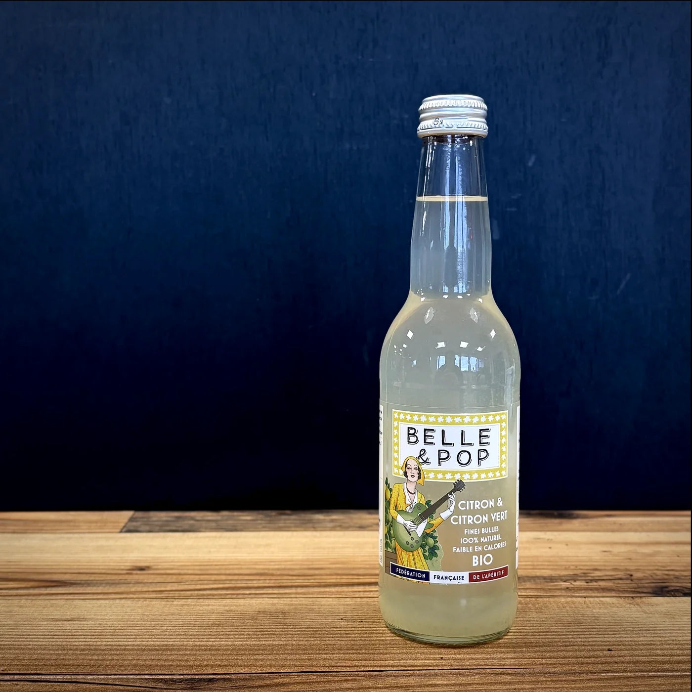 Belle & Pop Citron et Citron Vert BIO aux fines bulles, bouteille posée sur table en bois dans une ambiance apéritif naturelle et premium.