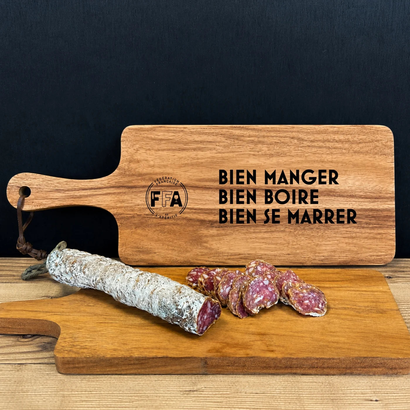 Planche apéritive FFA en bois avec le message “Bien manger bien boire bien se marrer” et saucisson sec tranché.