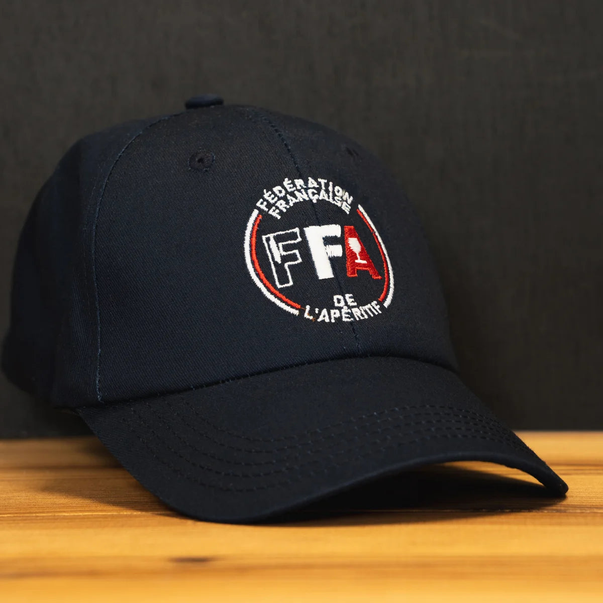 Casquette officielle FFA fabriquée en France, brodée avec le logo tricolore de la Fédération Française de l’Apéritif, posée sur une table en bois.