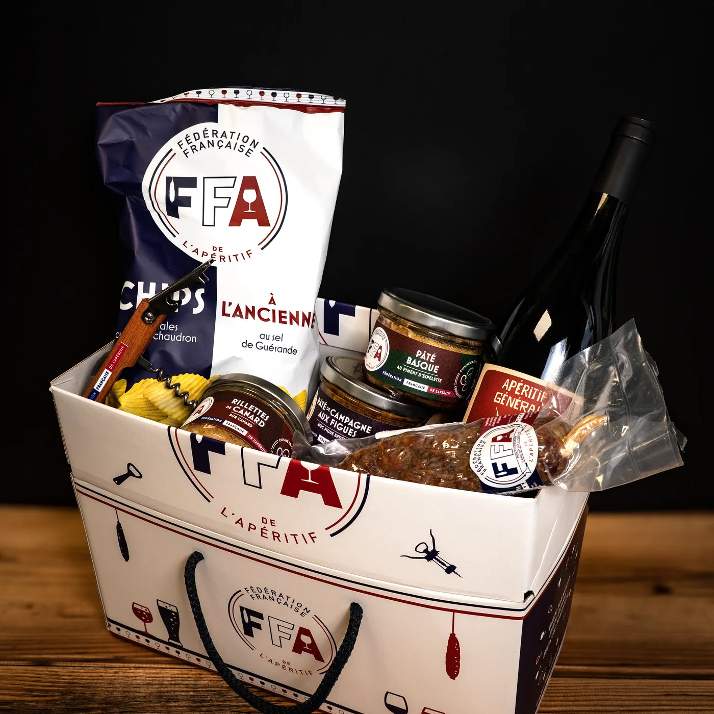 Coffret apéritif FFA garni de produits du terroir — chips, rillettes, pâté, vin rouge et saucisson, lumière chaleureuse et ambiance apéro.