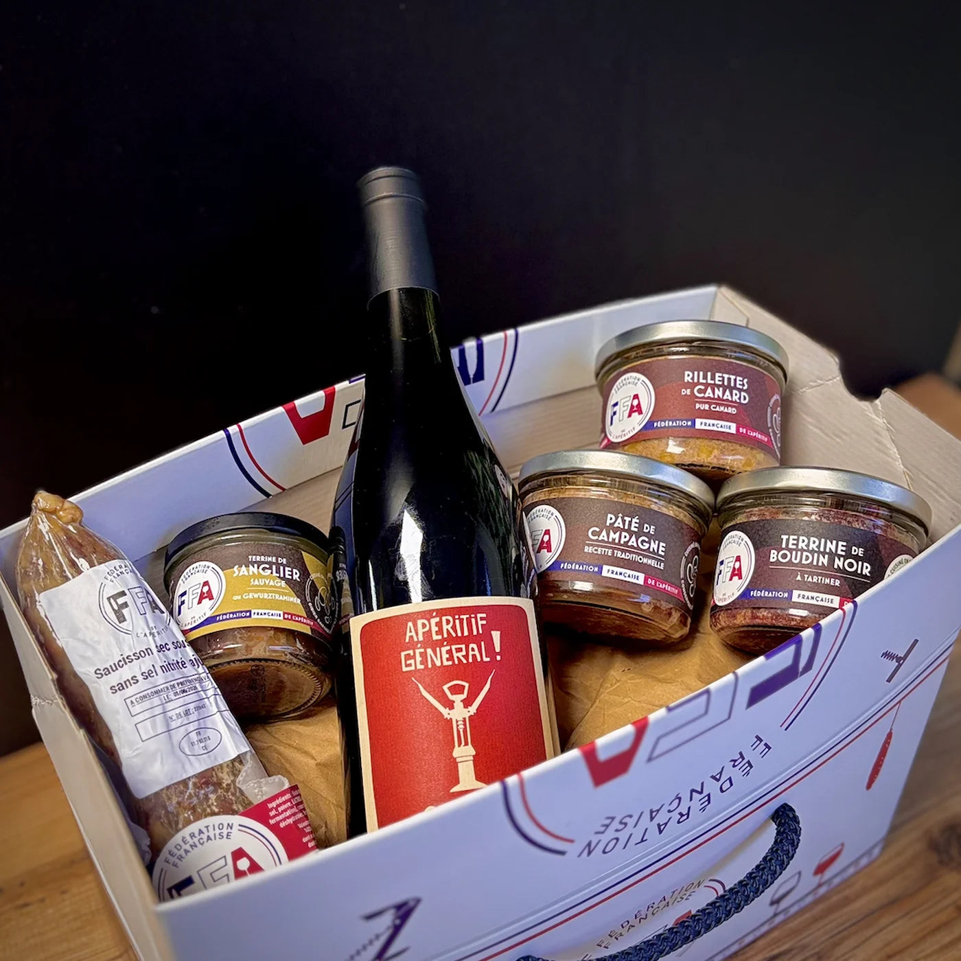 Intérieur du coffret apéritif FFA ouvert avec bouteille de vin rouge, terrines artisanales et rillettes, présentation généreuse et gourmande.