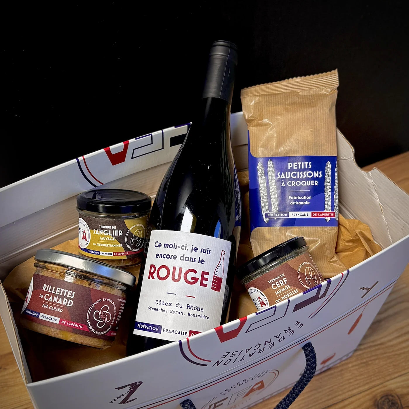 Coffret apéritif FFA ouvert avec vin rouge, terrines de gibier, rillettes de canard et saucissons à croquer, ambiance apéritif premium.