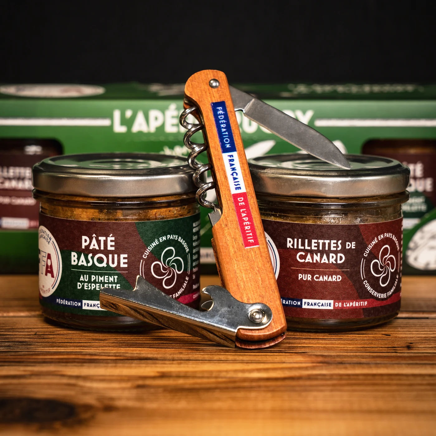 Pots de pâté basque et rillettes de canard FFA avec tire-bouchon en bois gravé Fédération Française de l’Apéritif, posés sur une table en bois — coffret L’Apéro Rugby gourmand et festif.