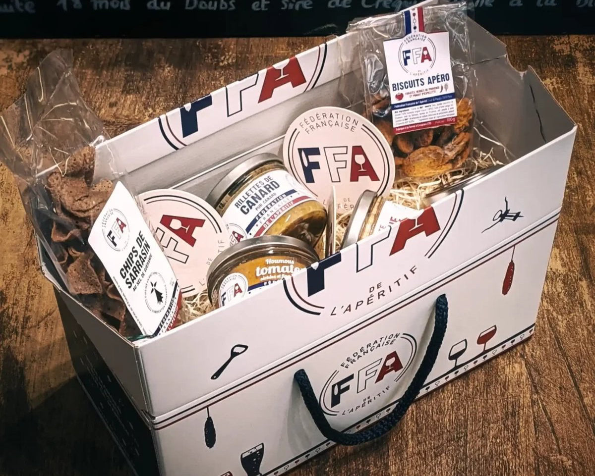 Coffret apéritif FFA garni de produits artisanaux, tartinables, biscuits et chips de sarrasin sur table en bois.