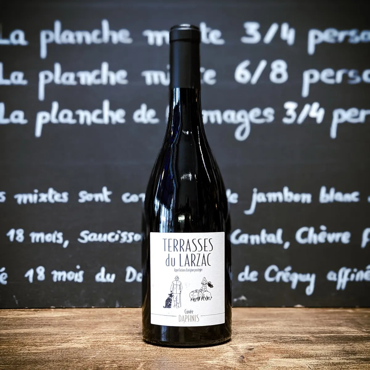 Bouteille de vin rouge Daphnis Terrasses du Larzac cuvée FFA, assemblage Syrah, Grenache et Carignan, vin artisanal du Languedoc exposé sur table en bois.