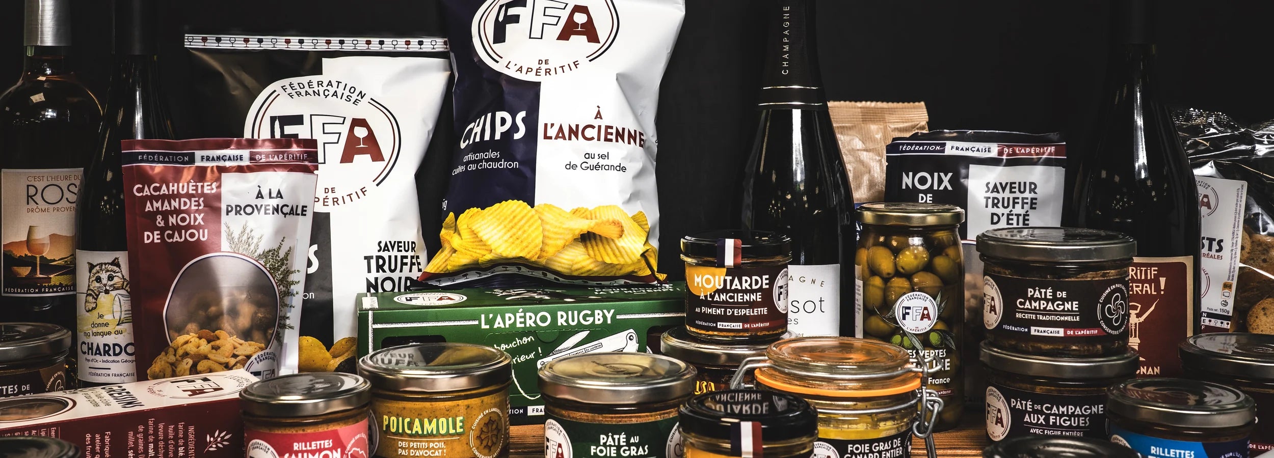 Large sélection de produits apéritifs FFA : vins, champagnes, chips, tartinables et charcuteries artisanales présentés sur une table en bois — Fédération Française de l’Apéritif.