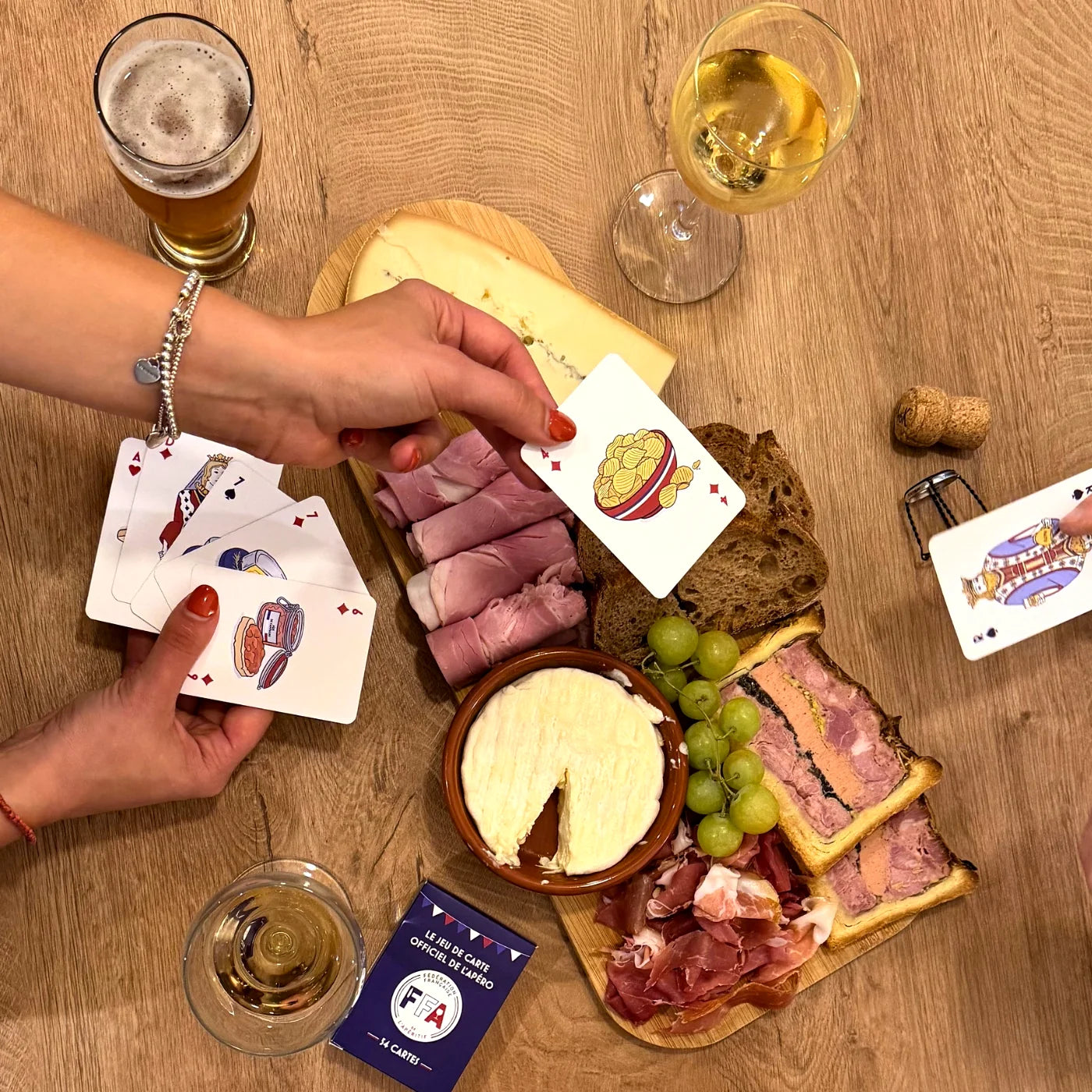 Jeu de cartes FFA étalé sur une table avec planche apéro composée de fromage, charcuterie et raisins — ambiance gourmande
