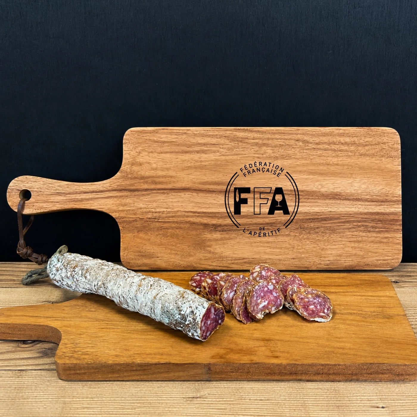 Grande planche à découper en bois gravée du logo de la Fédération Française de l’Apéritif, accompagnée d’un saucisson sec.