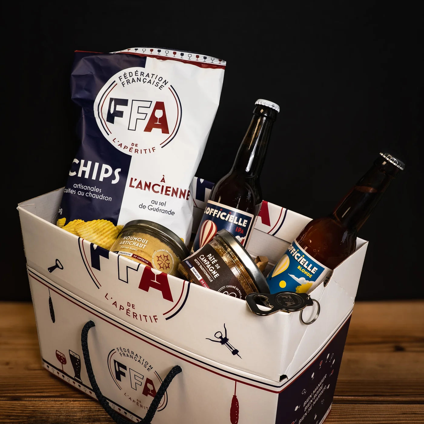 Panier cadeau FFA rempli de produits apéritifs avec chips, bières, pâté et houmous — collection “Apéro Vélo”.