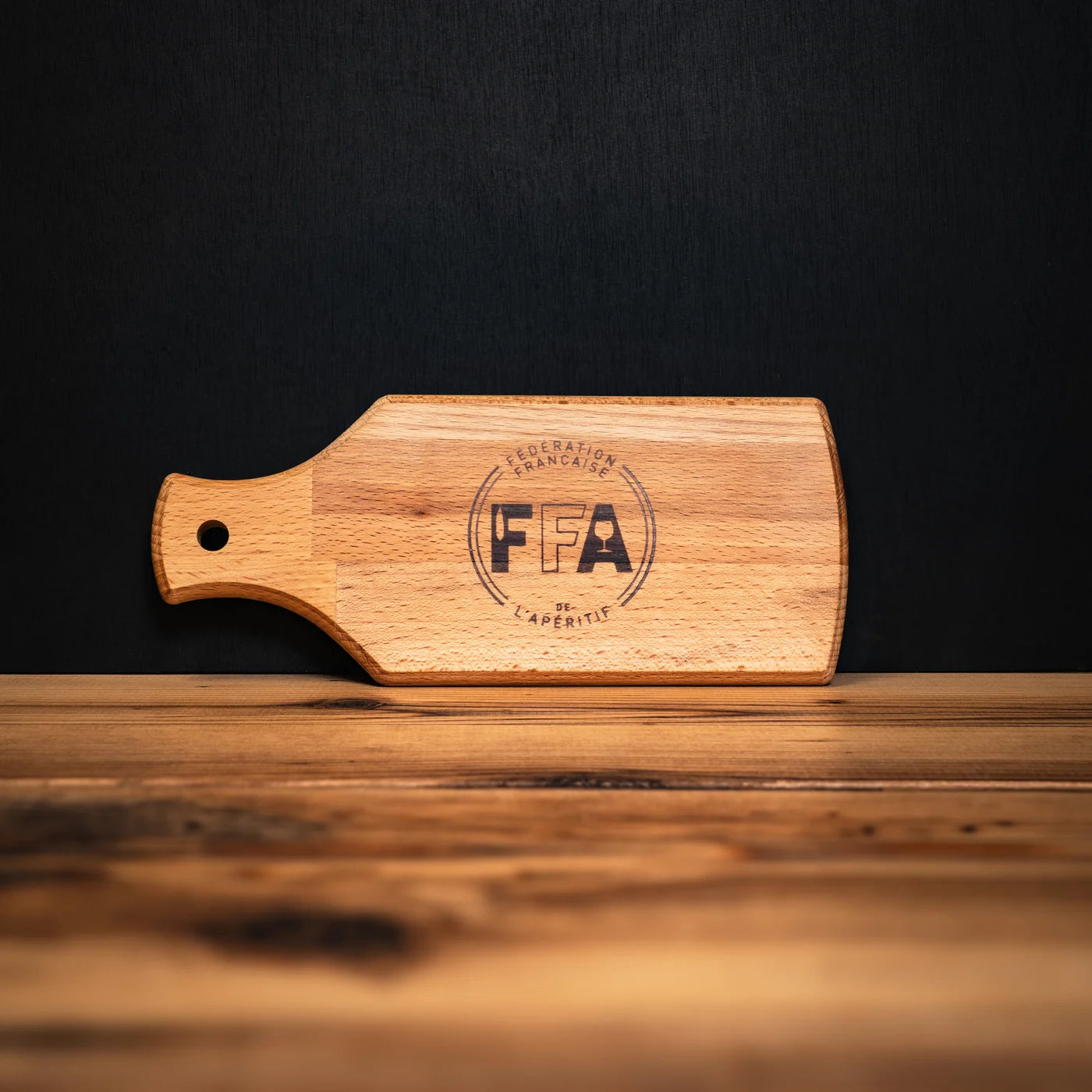Planche en bois gravée du logo de la Fédération Française de l’Apéritif, posée sur un comptoir en bois clair — un accessoire convivial et authentique pour sublimer l’apéro.