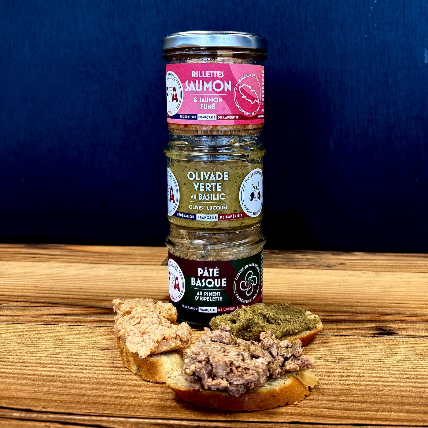 Trio de tartinables FFA – rillettes de saumon fumé, olivade verte au basilic et pâté basque au piment d’Espelette – présentés sur table en bois avec toasts gourmands, ambiance apéritif conviviale et premium.