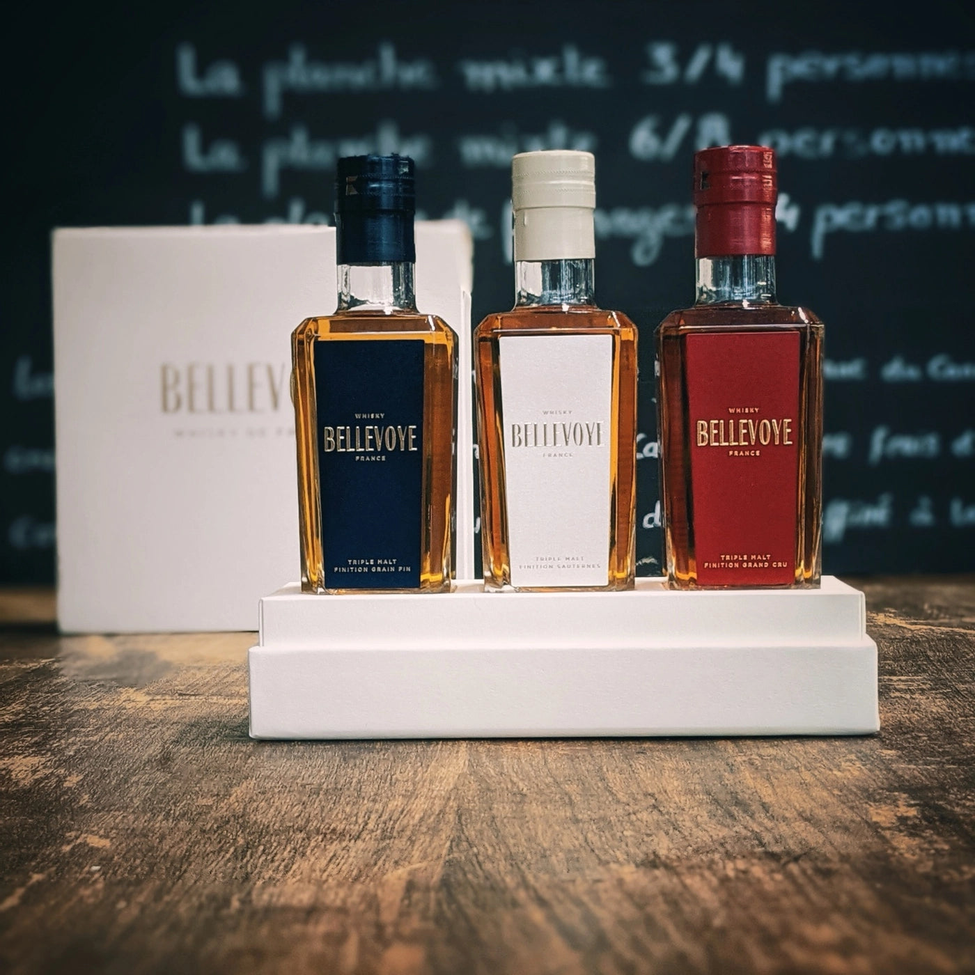 Coffret Bellevoye avec trois bouteilles de whisky français bleu, blanc et rouge, posé sur une table en bois, ambiance apéritif élégante et chaleureuse.