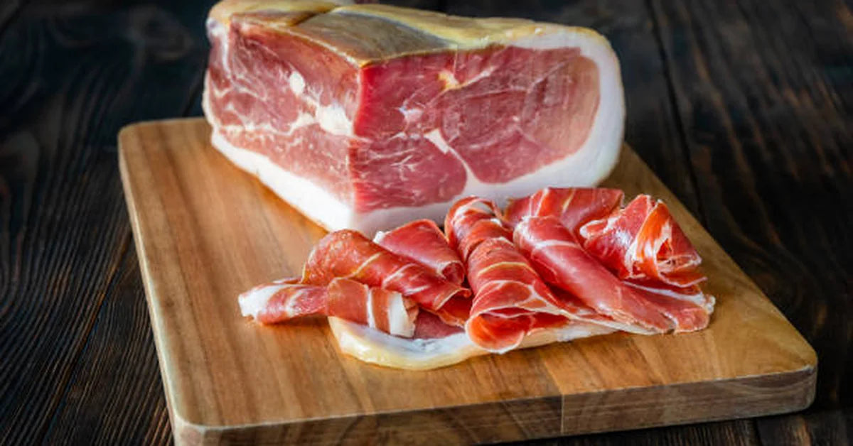 Morceau de jambon sec et lamelles finement tranchées posés sur une planche en bois, ambiance chaleureuse et gourmande