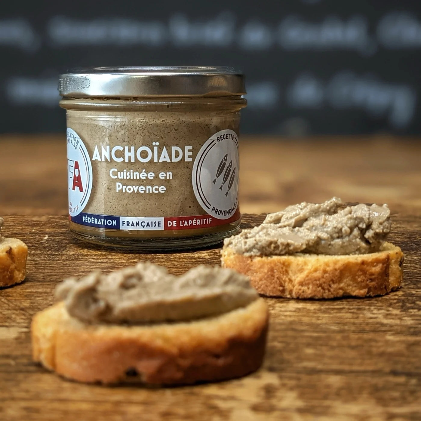 Bocal d’anchoïade FFA cuisinée en Provence posé sur une planche en bois avec toasts tartinés — ambiance apéritive artisanale et conviviale.