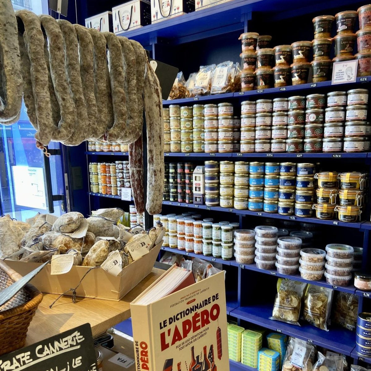Rayon épicerie de la boutique FFA avec saucissons, conserves artisanales et le livre Le Dictionnaire de l’Apéro.