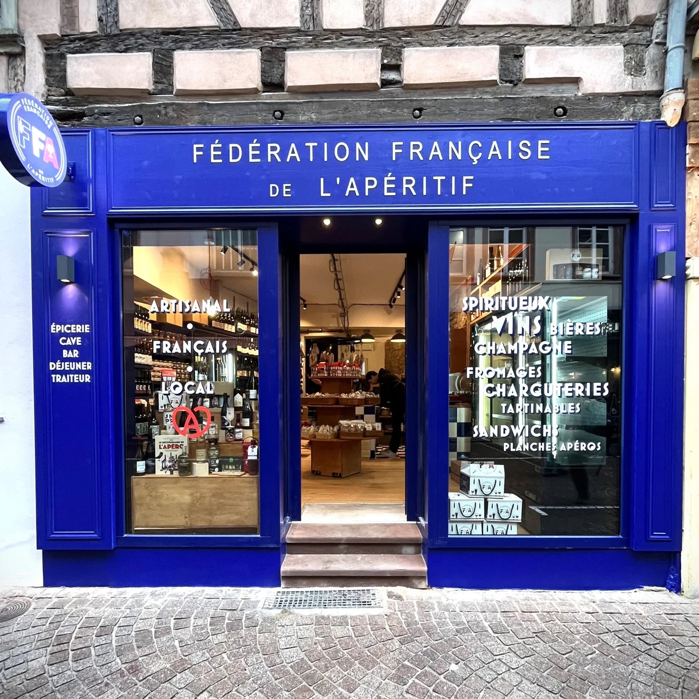 Façade bleue de la boutique Fédération Française de l’Apéritif à Strasbourg avec vitrine lumineuse et enseigne FFA — ambiance artisanale et conviviale.