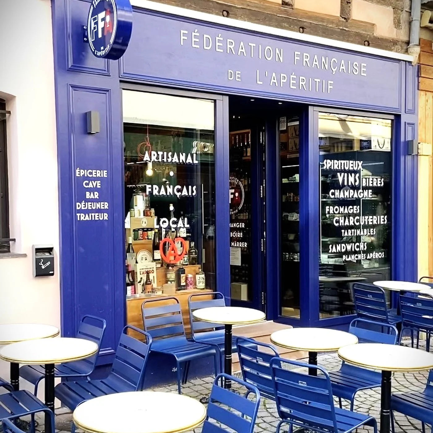 Façade bleue de la boutique Fédération Française de l’Apéritif à Strasbourg avec terrasse extérieure et tables bleues — ambiance conviviale et artisanale.