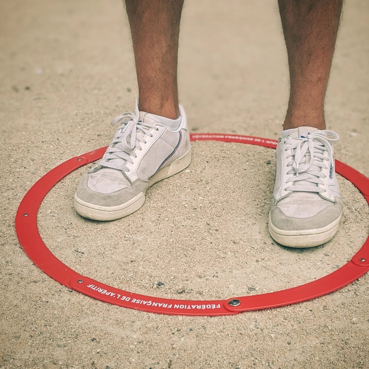 Cercle de pétanque rouge FFA fabriqué en France, posé sur un terrain de jeu, avec un joueur prêt à tirer.