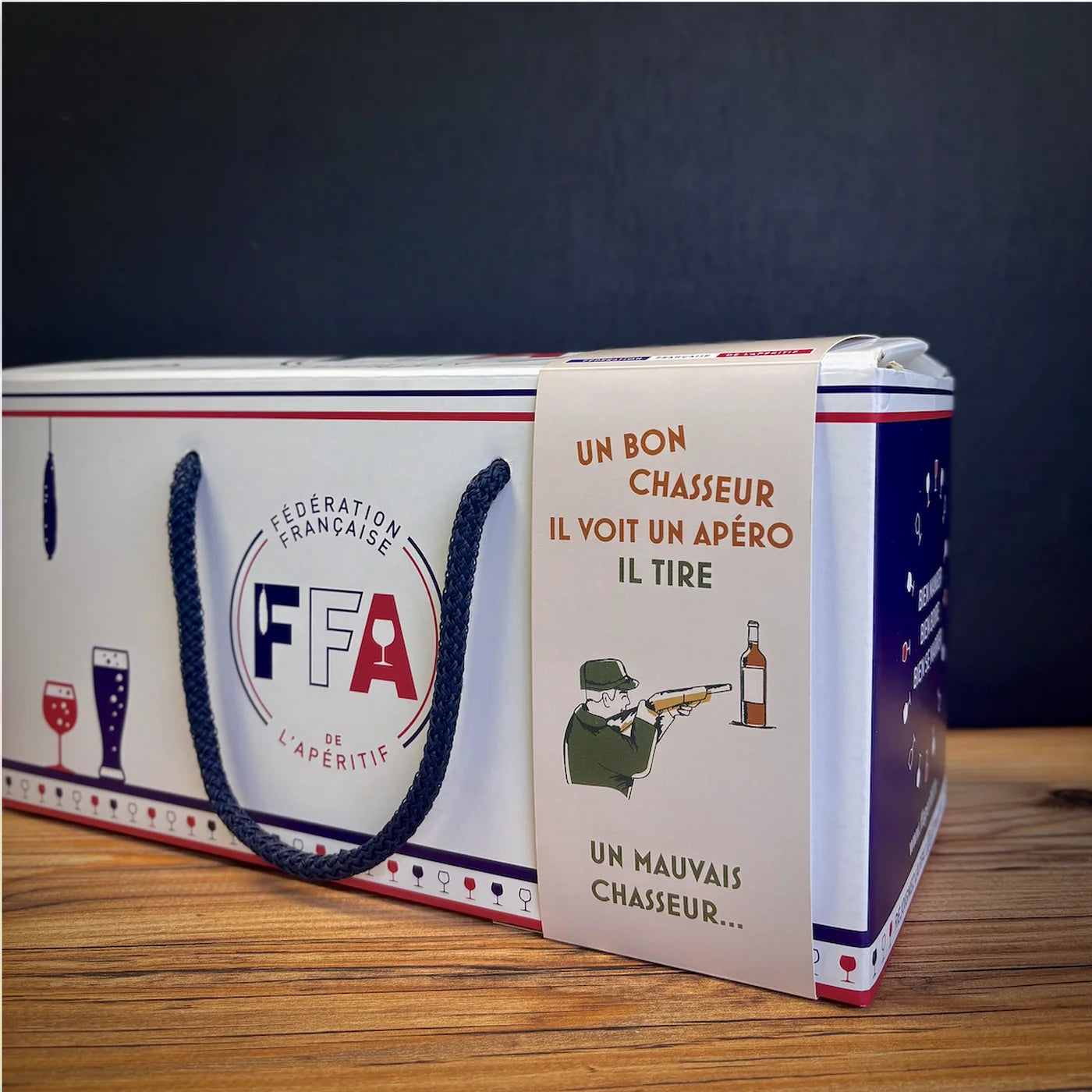 Coffret apéritif FFA avec message humoristique sur la chasse, coffret cadeau blanc premium avec cordage bleu, ambiance apéritive conviviale.