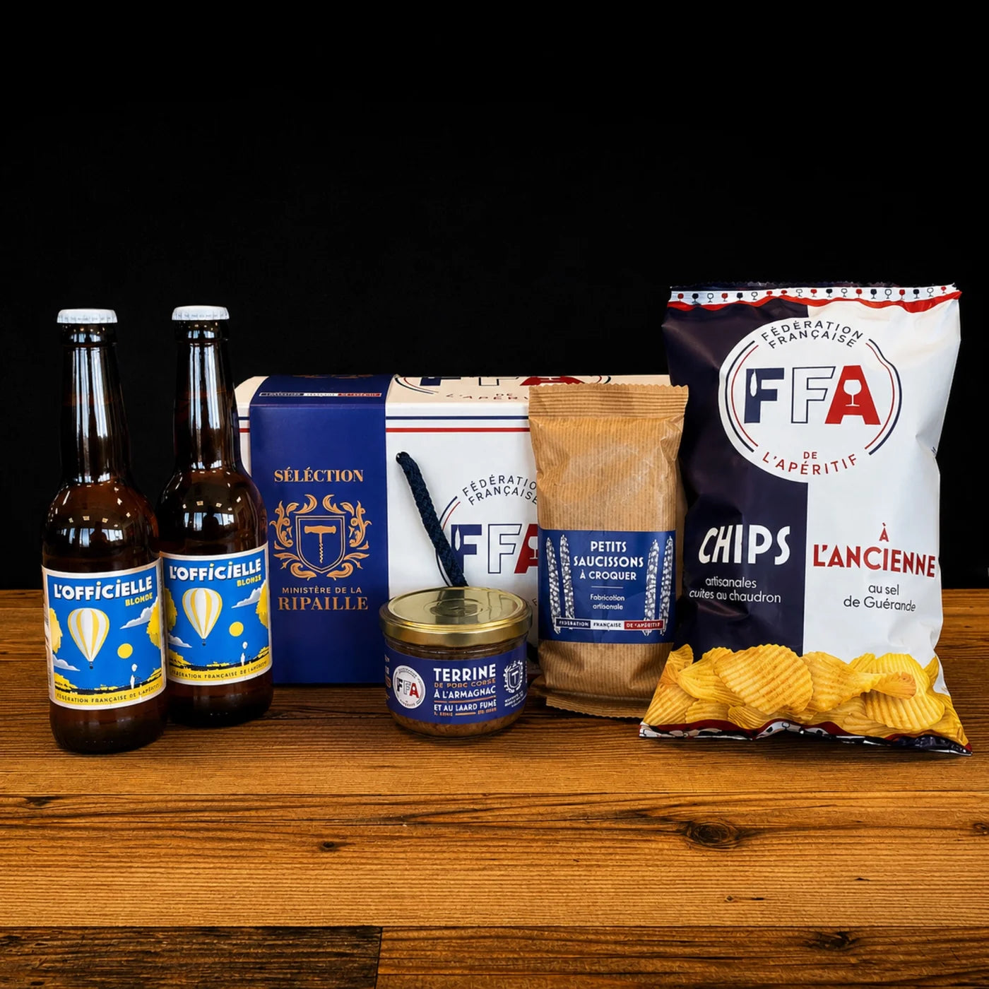 Coffret apéritif Fédération Française de l’Apéritif avec bières blondes artisanales, terrine à l’Armagnac, mini saucissons et chips artisanales au sel de Guérande sur table en bois. 