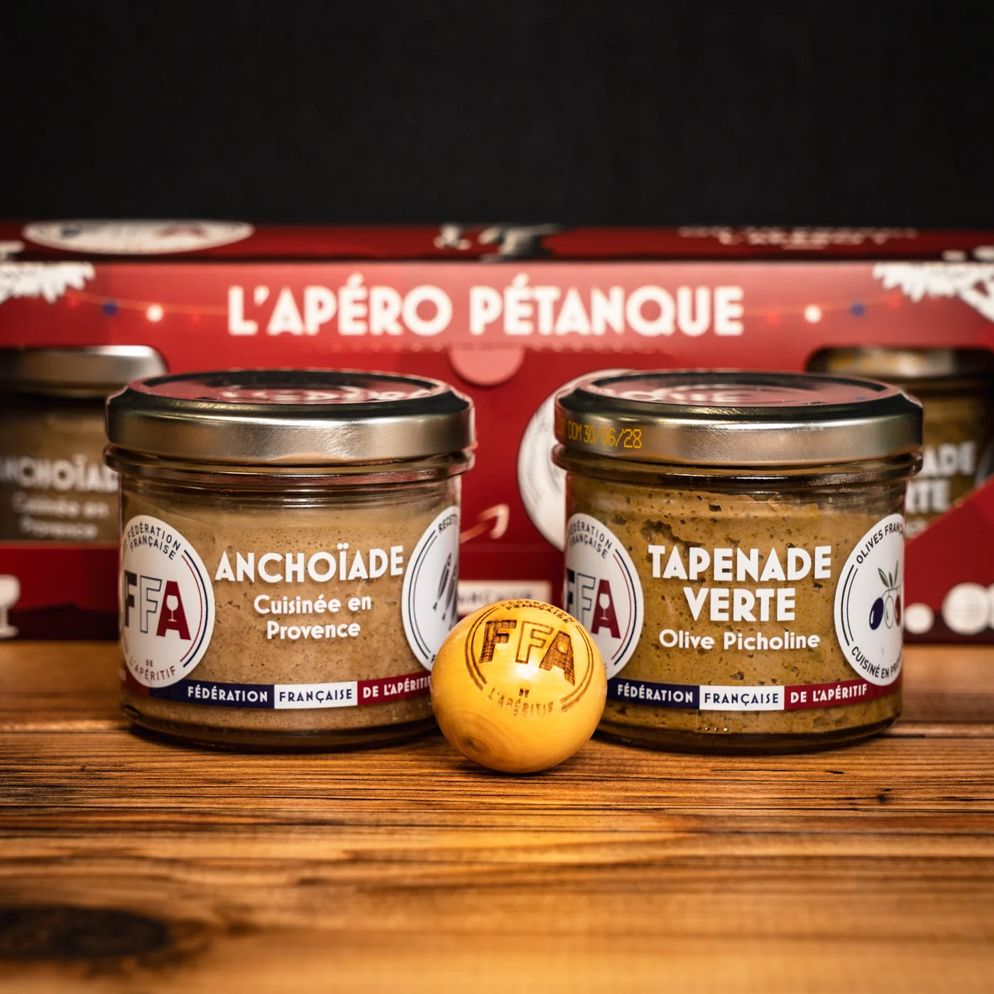 Pots d’anchoïade et de tapenade verte FFA avec cochonnet gravé FFA, posés sur une table en bois — coffret L’Apéro Pétanque convivial et gourmand.