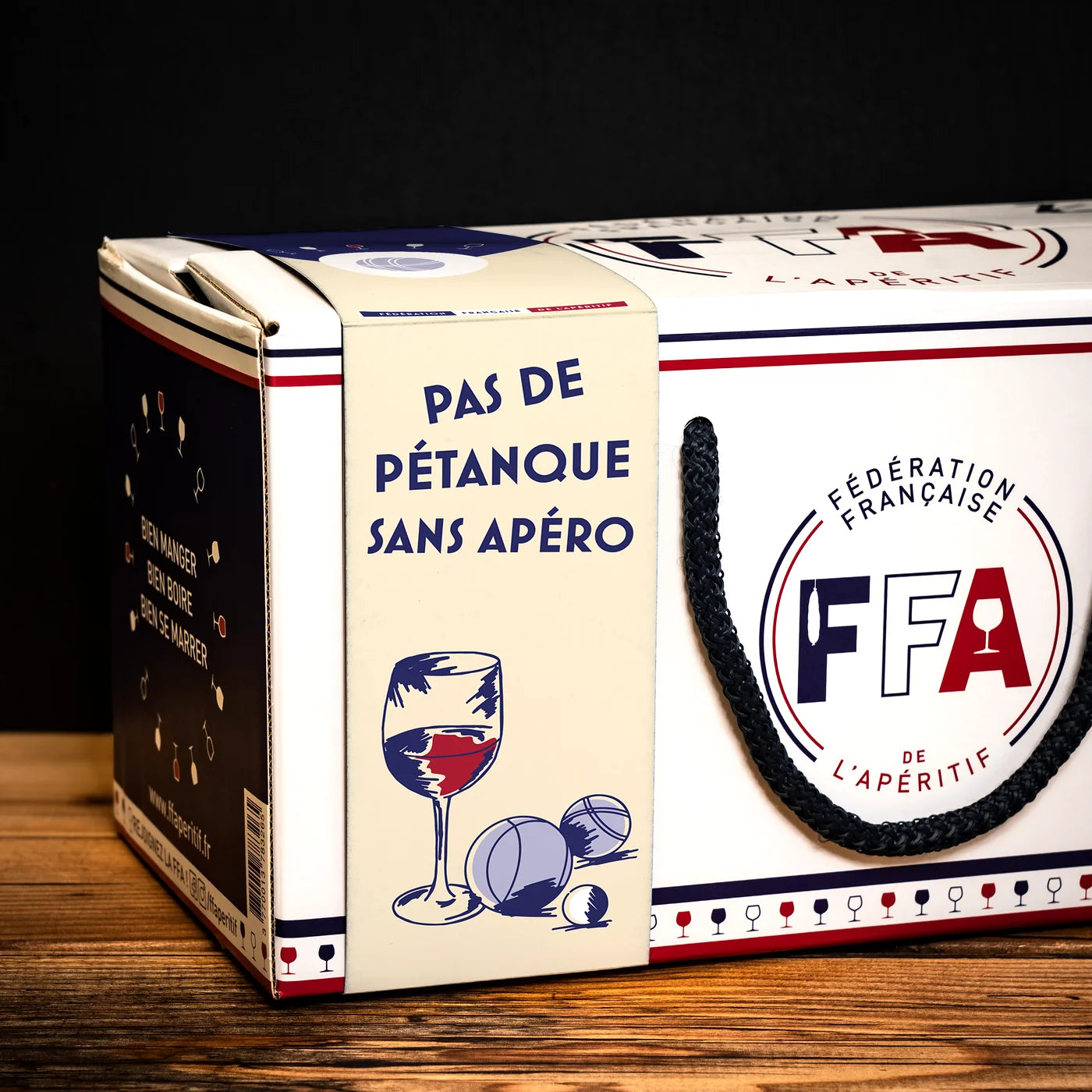 Face du coffret FFA avec l’illustration “Pas de pétanque sans apéro”, décor verres et boules de pétanque sur fond bois.