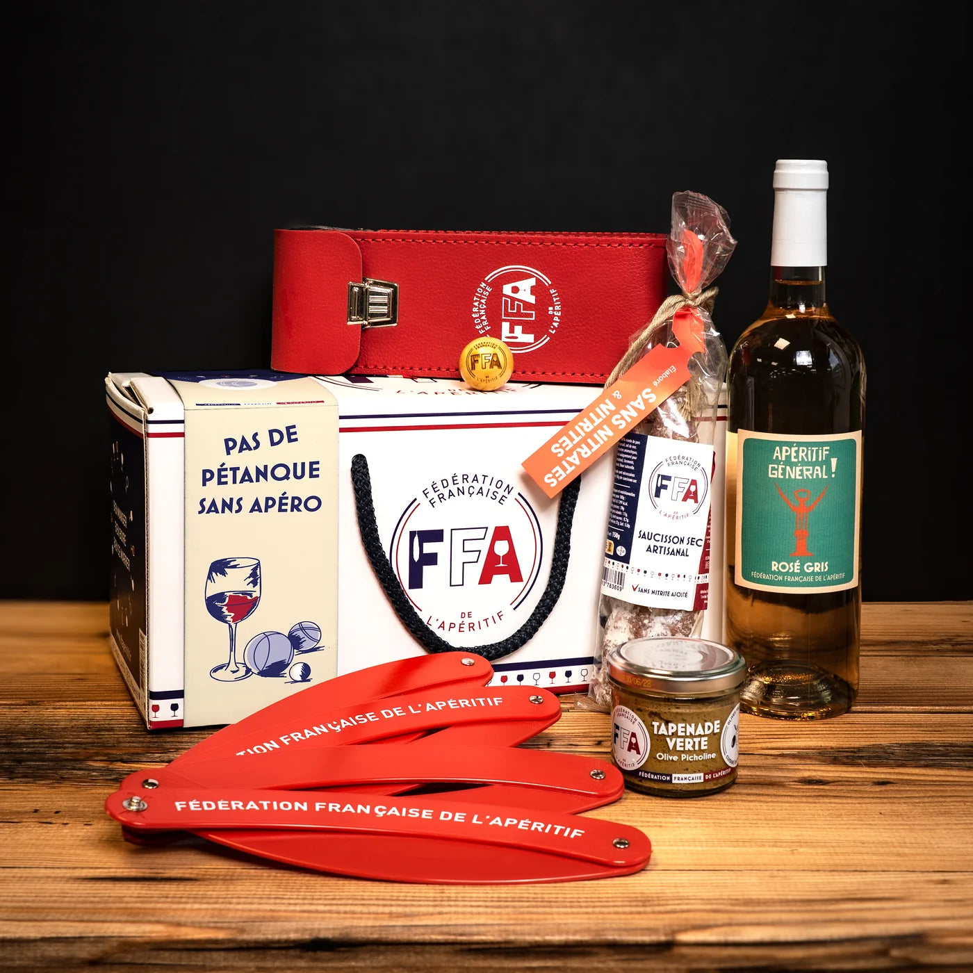 Coffret apéritif FFA accompagné de produits artisanaux — rosé gris, saucisson, tapenade et accessoires rouges FFA, ambiance conviviale sur fond bois.