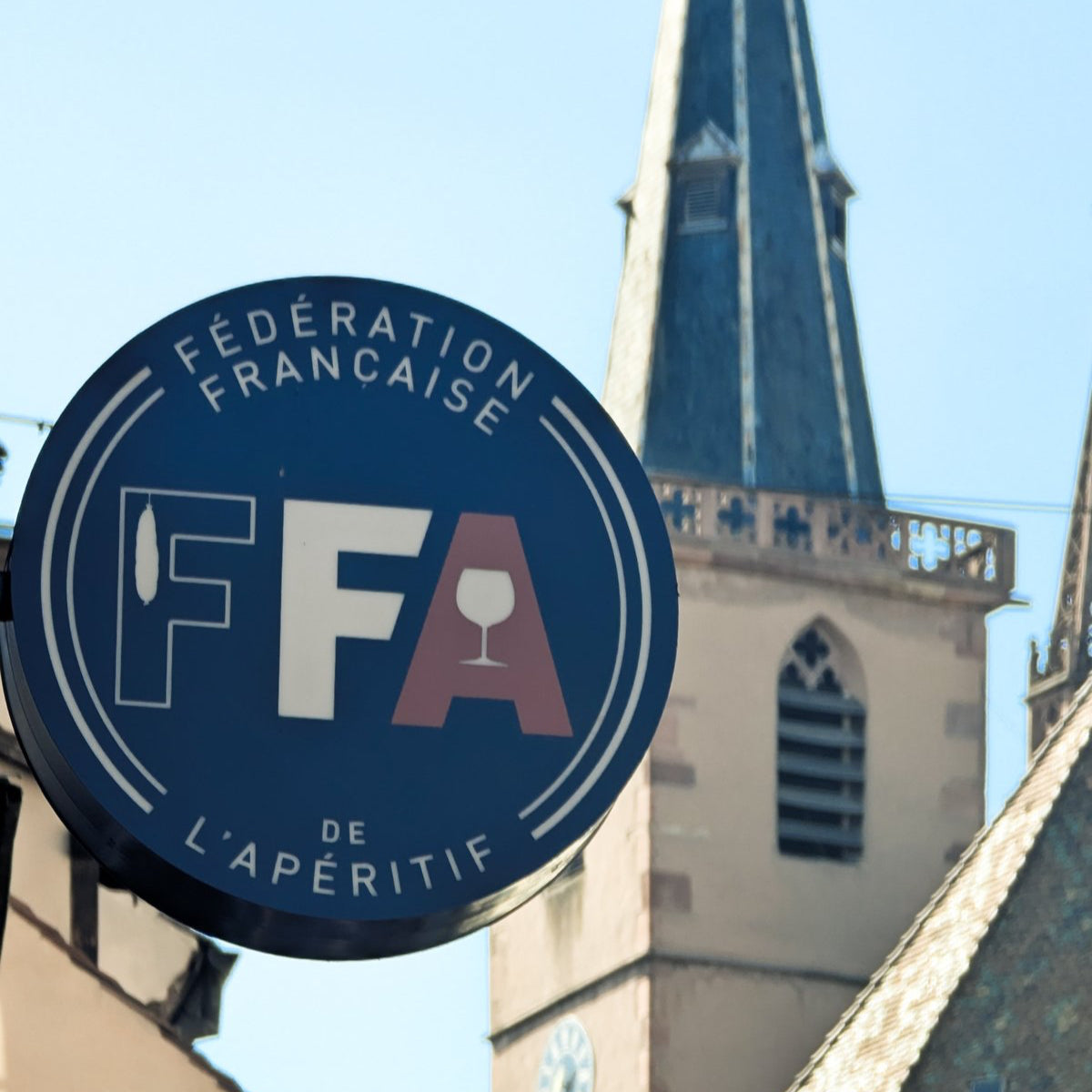 Enseigne de la Fédération Française de l’Apéritif à Strasbourg, devant l’église et les toits traditionnels de la ville.