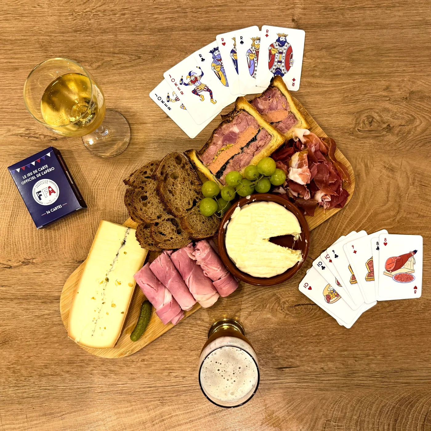 Coffret du jeu de cartes FFA posé sur une table en bois avec cartes et bouchon de champagne — ambiance apéritif conviviale