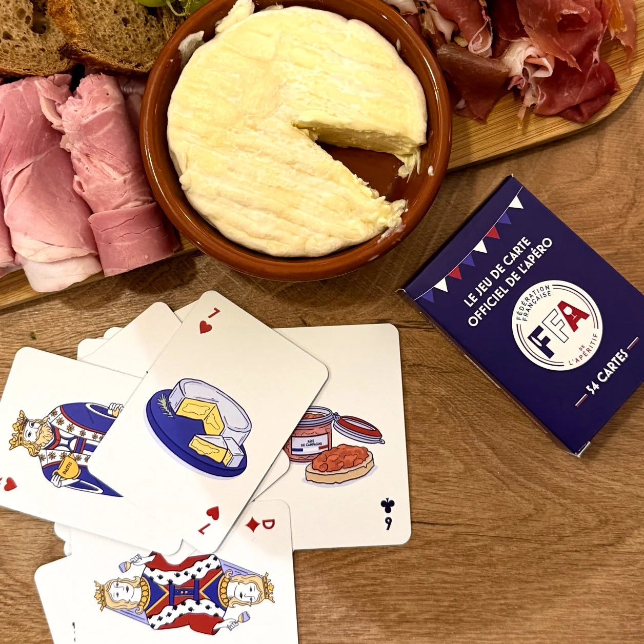 Coffret du jeu de cartes FFA posé sur une table en bois avec cartes et bouchon de champagne — ambiance apéritif conviviale