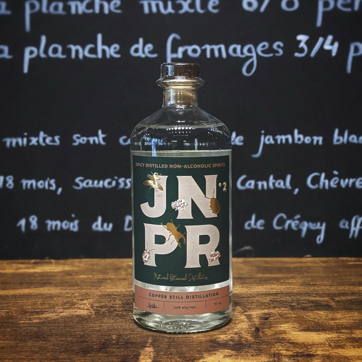 Bouteille de spiritueux sans alcool JNPR n°2 posée sur un comptoir en bois, étiquette verte élégante et ambiance de bar chaleureuse pour un apéritif moderne et raffiné.