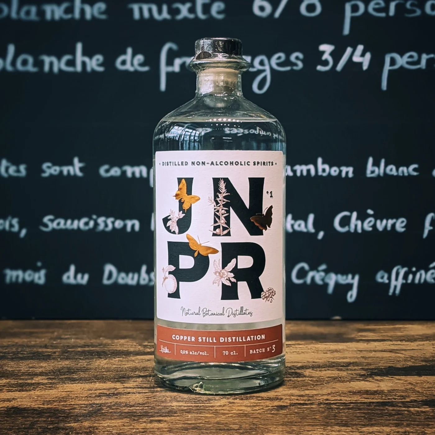Bouteille de spiritueux sans alcool JNPR posée sur un comptoir en bois, étiquette botanique élégante et ambiance de bar raffinée pour un apéritif moderne et convivial.