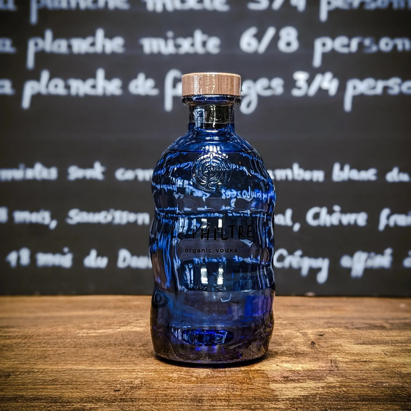 Bouteille de vodka Laphtrè bleue en verre ondulé, posée sur un comptoir en bois avec un fond ardoise de type épicerie fine.