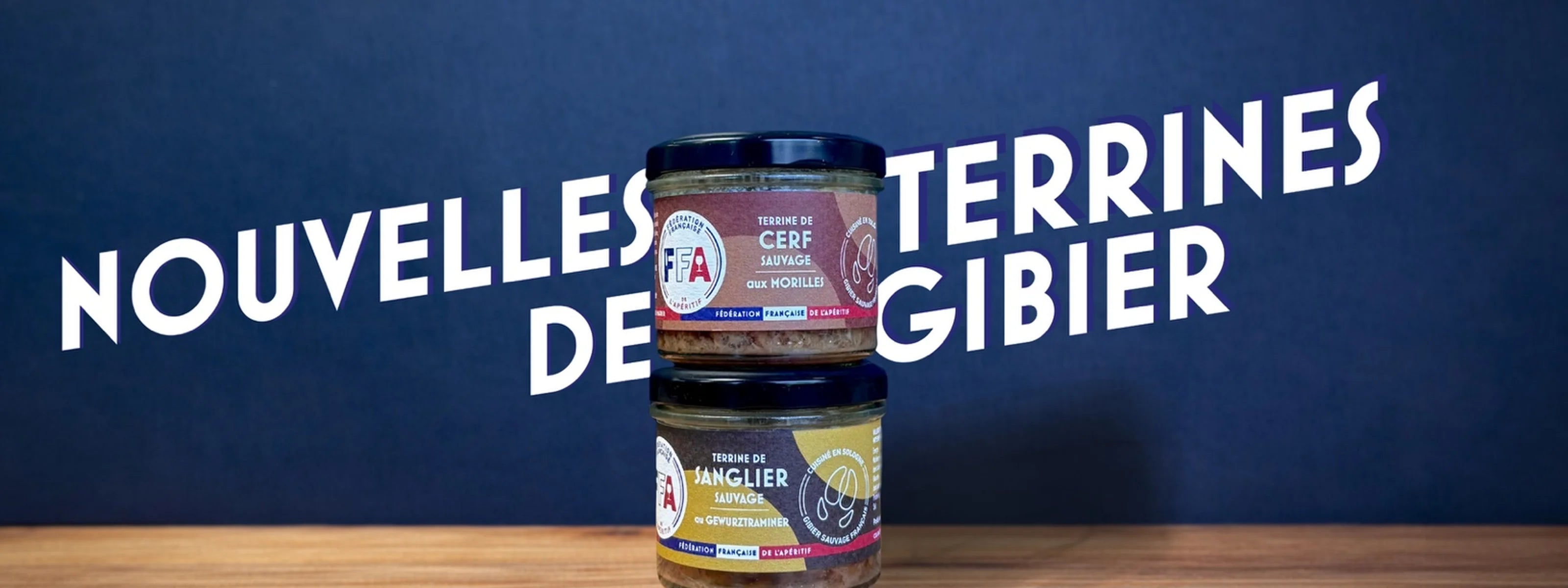 Nouvelles terrines de gibier FFA présentées en bocaux empilés sur une table en bois, terrines de cerf et de sanglier sur fond bleu, ambiance apéritive premium et gourmande.