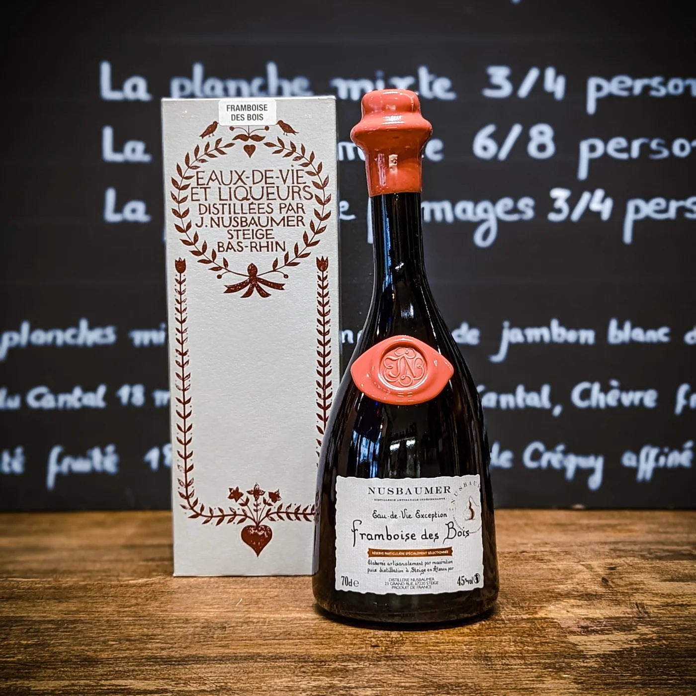 Bouteille d’eau-de-vie Framboise des Bois Nusbaumer avec son coffret en bois clair, posée sur un comptoir — un spiritueux artisanal alsacien au charme authentique et gourmand.