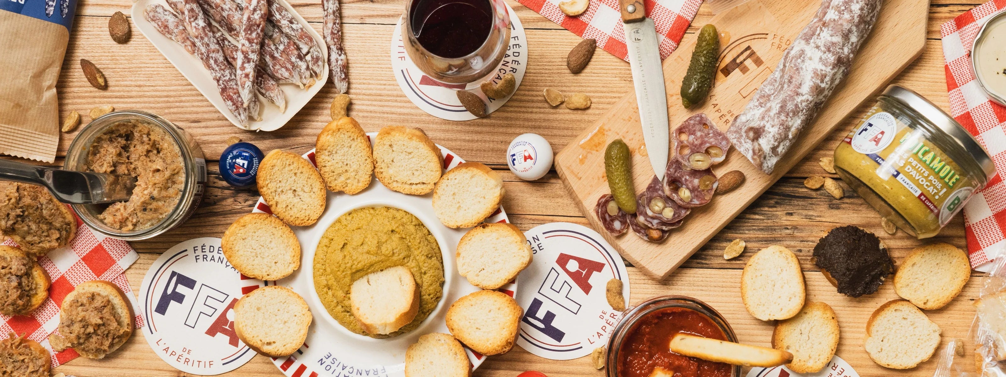Planche apéritive FFA avec saucisson, tartinables, gressins, toasts et verres de vin sur une table en bois — ambiance conviviale et gourmande à l’apéritif.