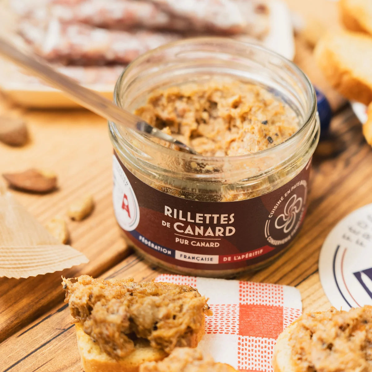 Bocal de rillettes de canard FFA posé sur une table en bois avec toasts croustillants — ambiance gourmande et artisanale de l’apéritif.