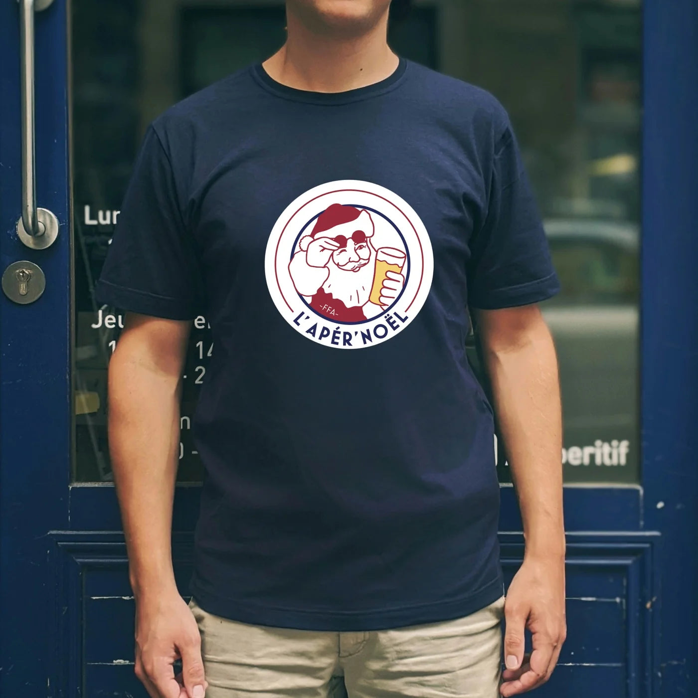 T-shirt bleu FFA “L’Apèr’Noël” porté devant une devanture bleue, avec illustration du Père Noël à l’apéro.