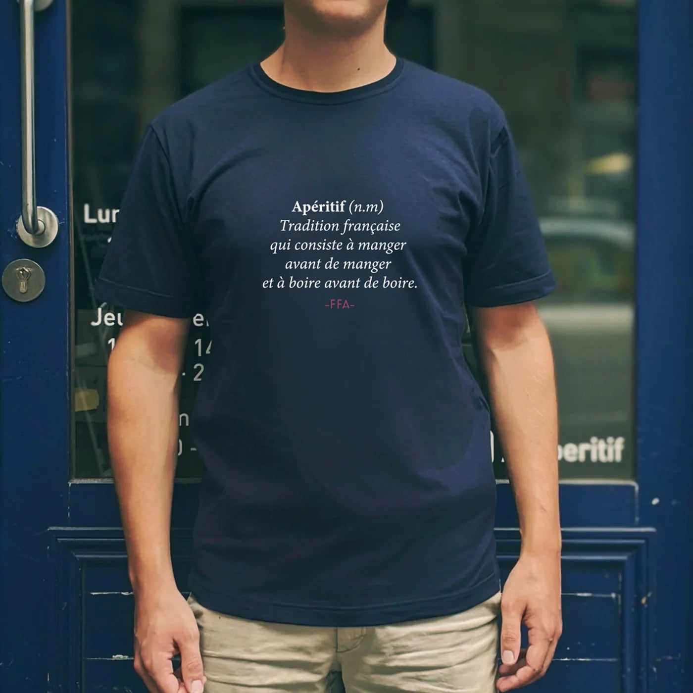 T-shirt bleu FFA avec définition humoristique de l’apéritif, porté devant une devanture bleue — rendu clair, moderne et convivial.