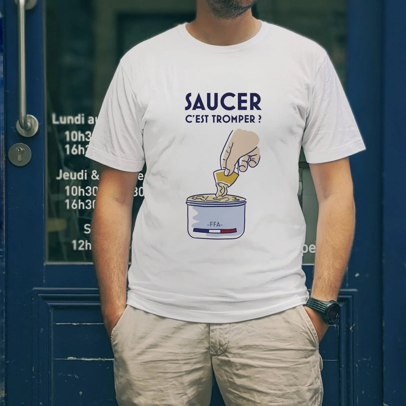 T-shirt blanc FFA “Saucer c’est tromper ?” avec illustration humour apéritif, porté devant une devanture bleue.