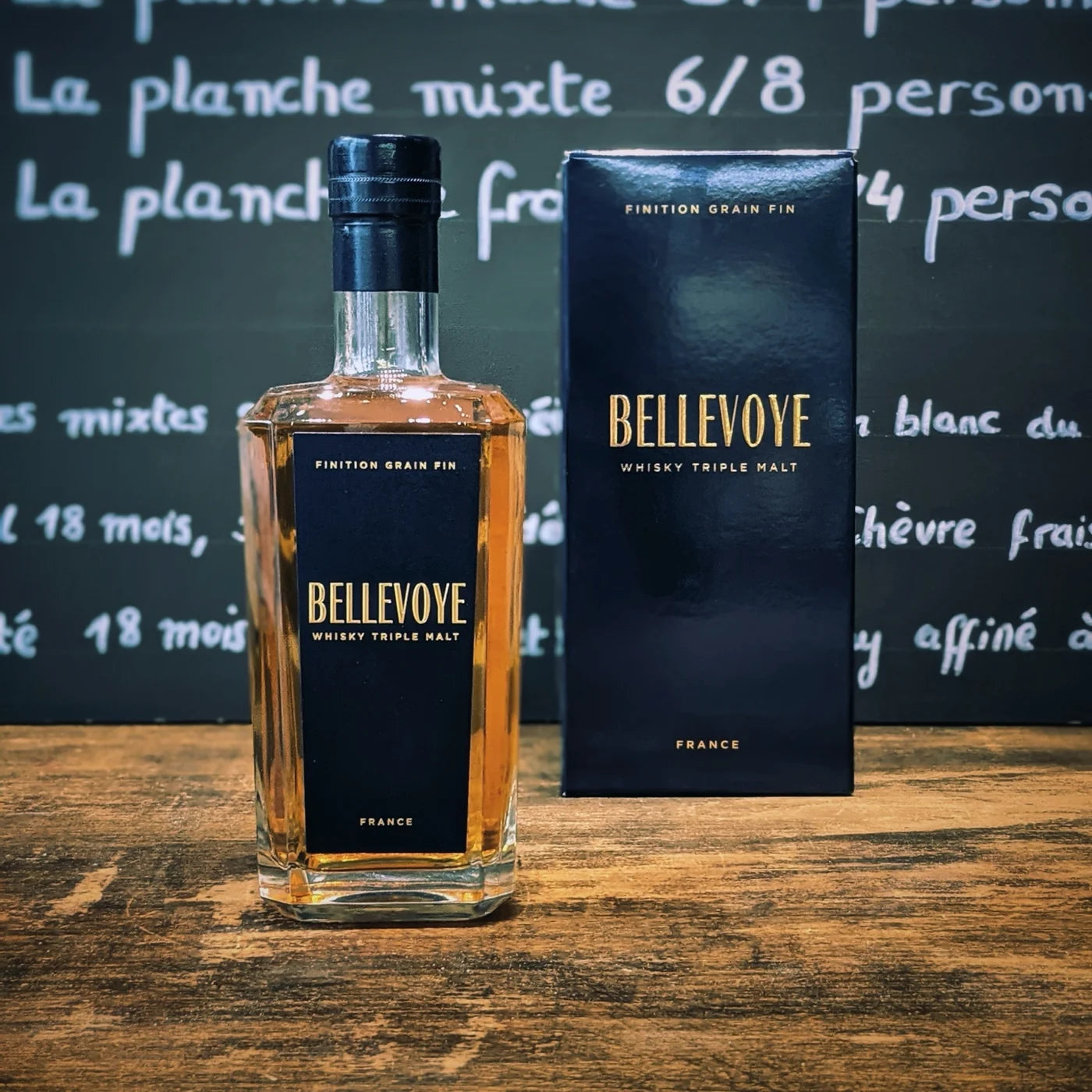 Bouteille de whisky Bellevoye Triple Malt finition grain fin avec son coffret bleu marine, posée sur un comptoir en bois — un spiritueux français d’exception à savourer à l’apéritif.